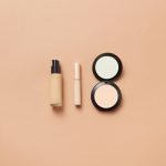 Flatlay of foundation, concealer, and compact powder on beige background. Perfect for beauty and cosmetic themes.