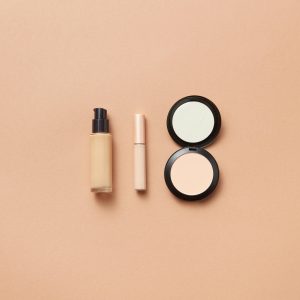 Flatlay of foundation, concealer, and compact powder on beige background. Perfect for beauty and cosmetic themes.